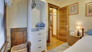 A bedroom with a wooden wardrobe, a bed with a blue pillow, a nightstand with a lamp, and a door leading to a staircase. - Charming Urbana Home Near Downtown! (Urbana)