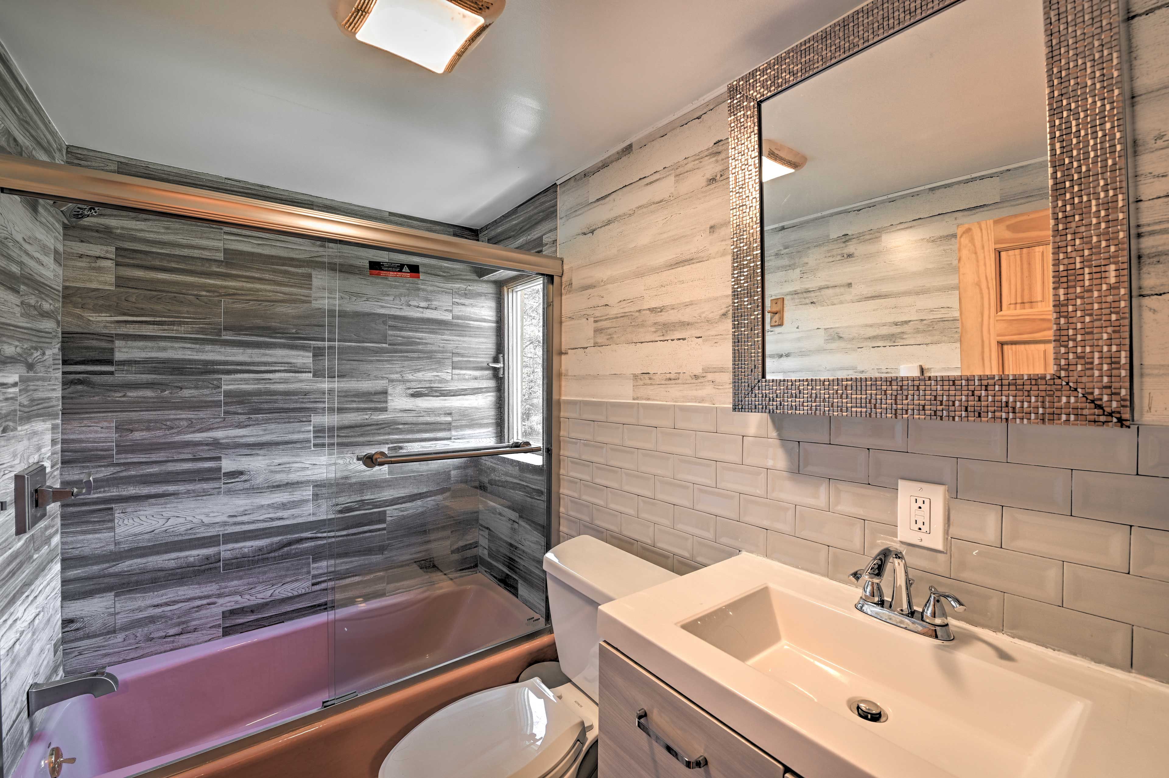 Un baño con cabina de ducha de vidrio, inodoro y lavamanos con espejo.
