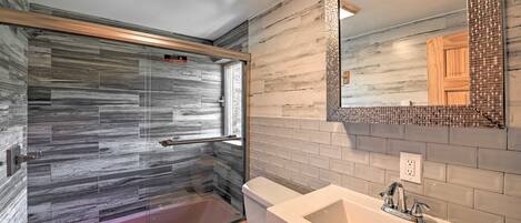 Un baño con cabina de ducha de vidrio, inodoro y lavamanos con espejo.