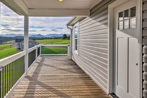 A wooden deck with a white railing, a door, and a view of a green landscape with mountains in the distance.