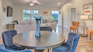 A spacious living room with a round table, blue chairs, a ceiling fan, and a large window offering a view of the outdoors. - Unique Blue Ridge Haven, 12 Mi to Asheville! (Leicester)