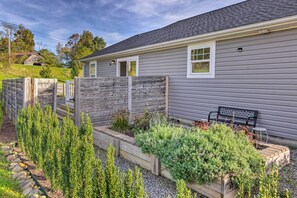 A residential property with a grey house, a wooden fence, a garden with various plants, and a bench. - Unique Blue Ridge Haven, 12 Mi to Asheville! (Leicester)
