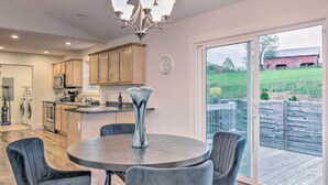 A modern kitchen with wooden cabinets, a round dining table with chairs, and a large window overlooking a deck. - Unique Blue Ridge Haven, 12 Mi to Asheville! (Leicester)