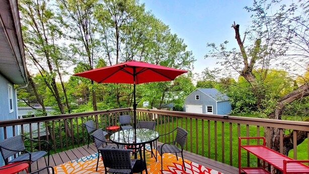 Une terrasse dotée de mobilier d’extérieur, d’une table en verre et d’un parasol rouge.