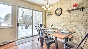 Un coin repas avec un mur en briques, une table en bois, des chaises noires et une horloge murale.