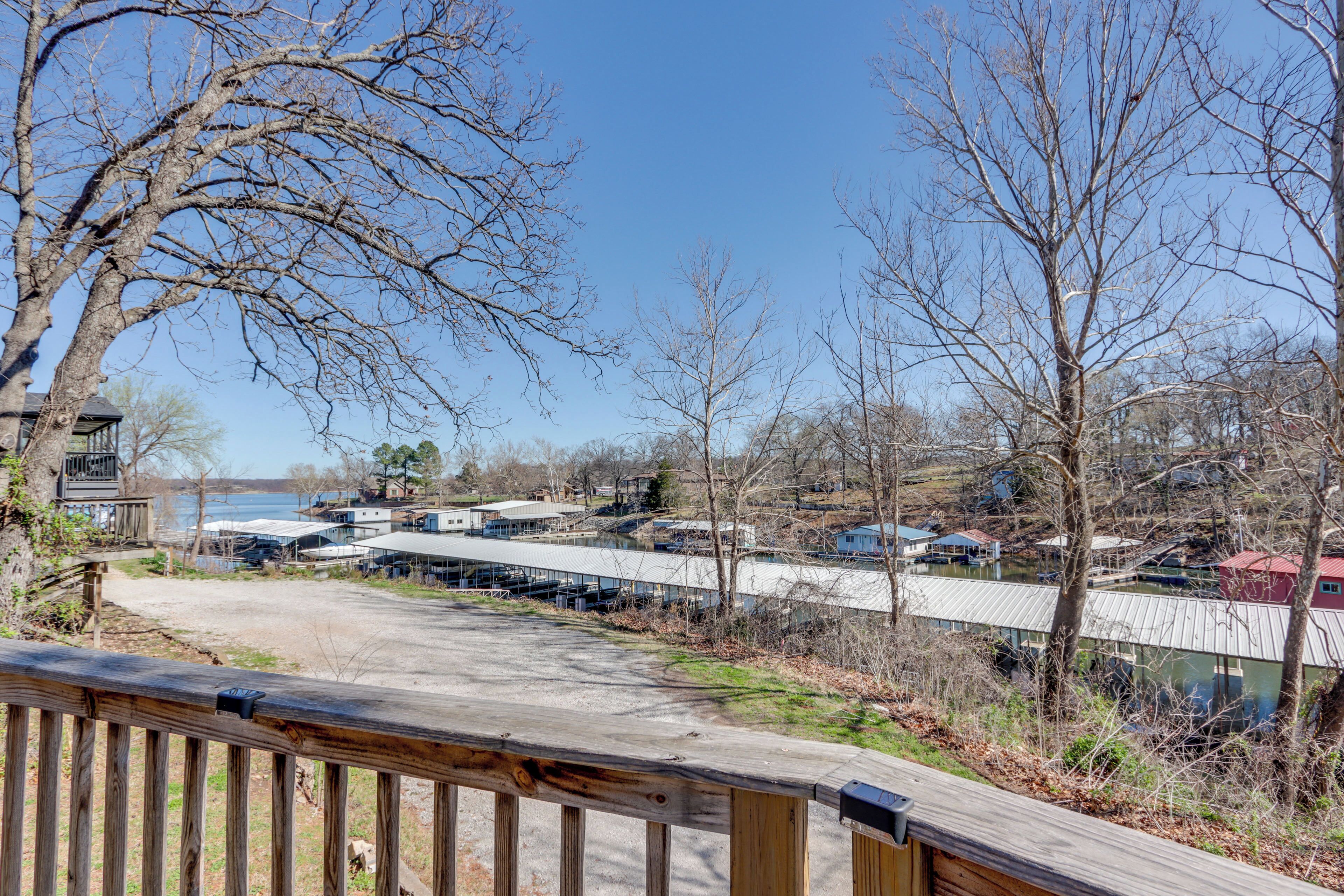 A view of a lakeside property with a wooden deck, a covered parking area, and buildings with a modern architectural style.