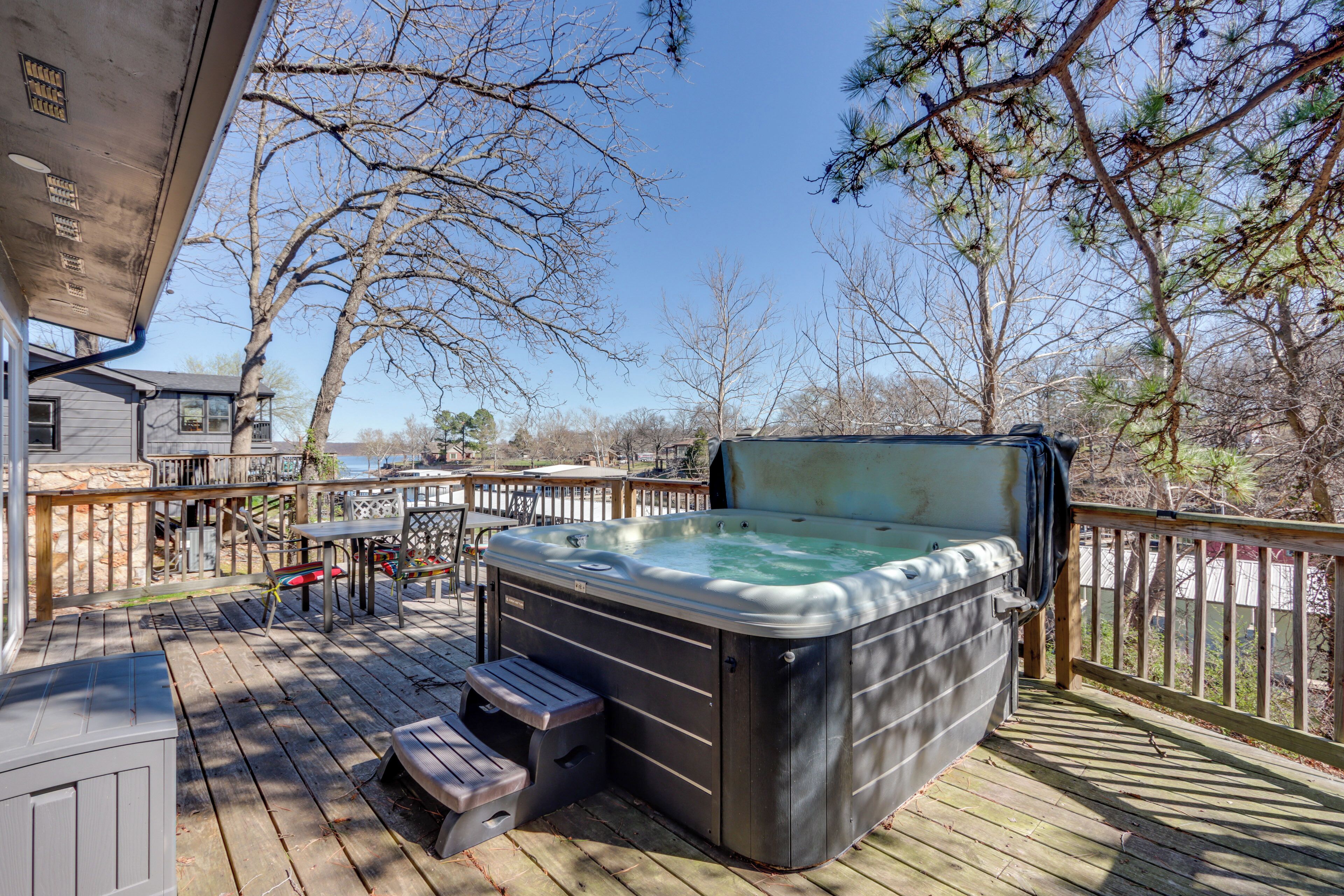 Een hottub op een houten terras, met uitzicht op bomen en een gebouw op de achtergrond.
