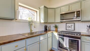 A kitchen with light blue cabinets, a stainless steel oven, a microwave, and a window with a plant.