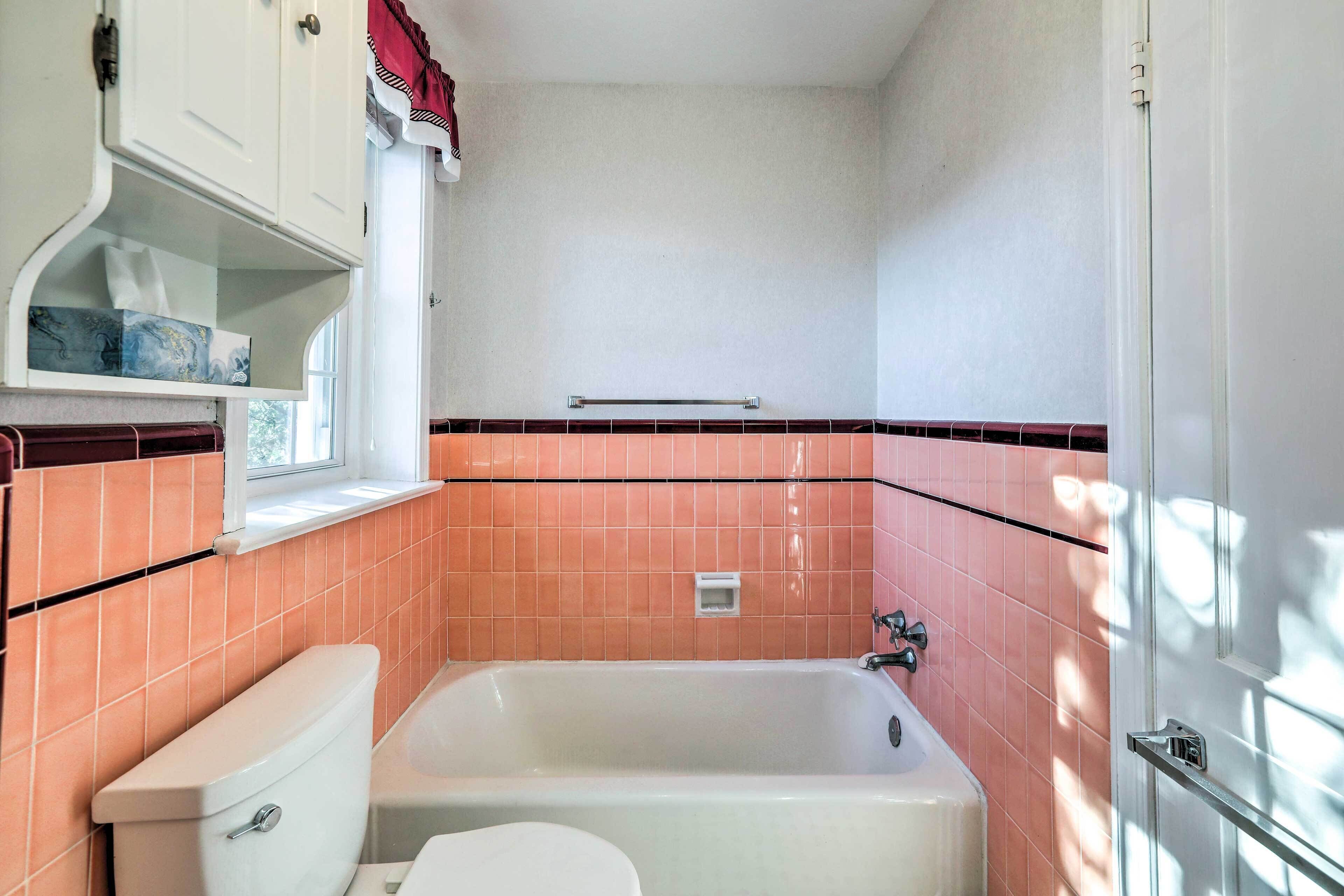 Ein Badezimmer mit Badewanne, Toilette und einem Fenster über dem Waschbecken.
