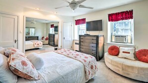 Une chambre à coucher avec un lit, une commode, un téléviseur et une fenêtre avec des rideaux.