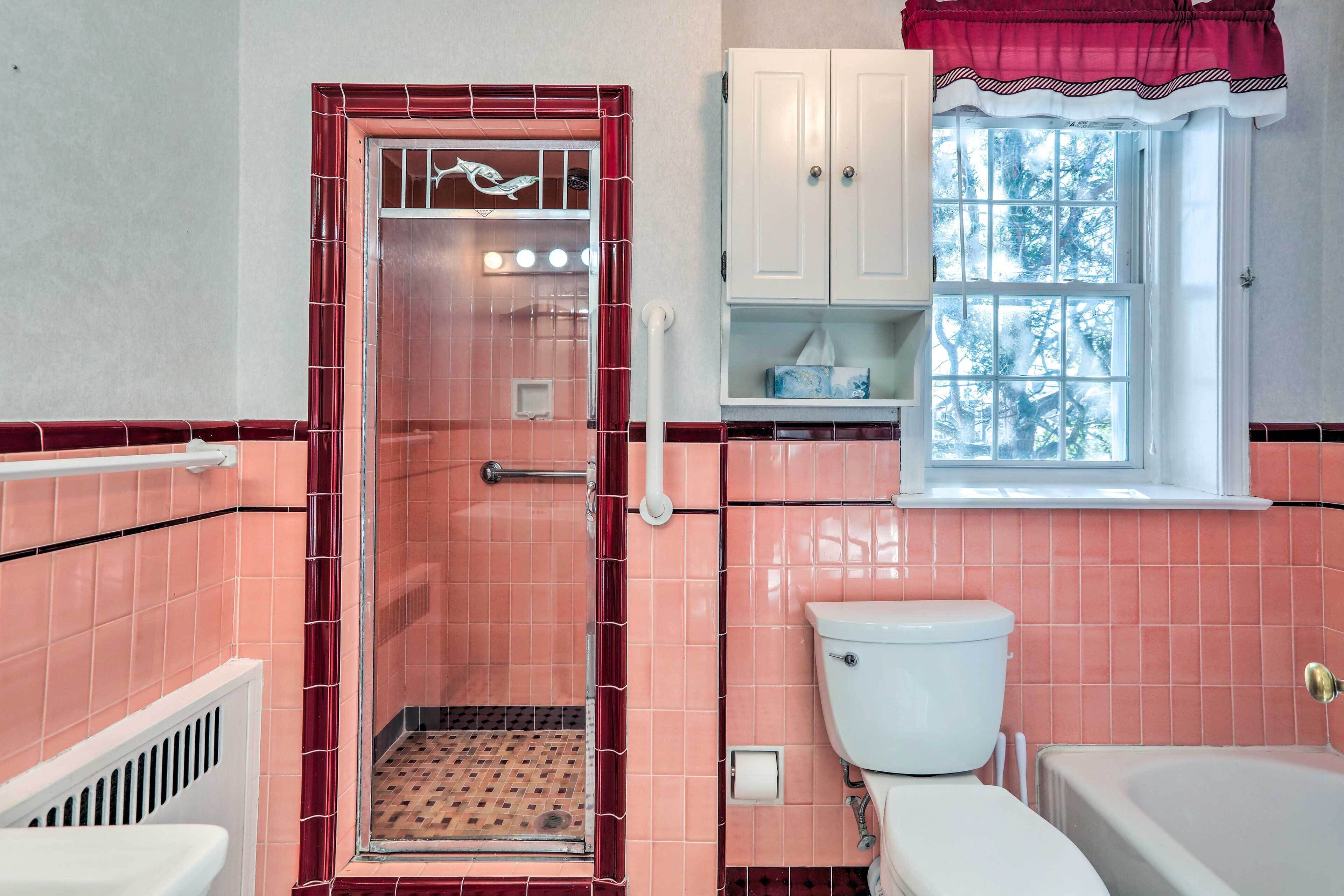 A bathroom with a walk-in shower, a toilet, a bathtub, and a window with a view of trees.