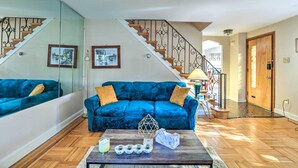Un salon doté d’un canapé en velours bleu, d’un parquet, d’une table basse agrémentée d’objets décoratifs et d’un escalier avec des rampes ouvragées.