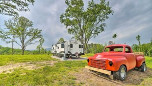 A red vintage car parked in a grassy field with a white RV in the background. - Updated Studio Cabin in Ozark w/ Yard & Mtn View (Ozark)