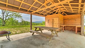A rustic wooden structure with a picnic table and benches, surrounded by a concrete floor and a view of greenery. - Updated Studio Cabin in Ozark w/ Yard & Mtn View (Ozark)
