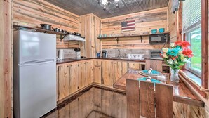 A rustic kitchen with wooden walls, a refrigerator, a microwave, and a dining area with a table and chairs. - Updated Studio Cabin in Ozark w/ Yard & Mtn View (Ozark)