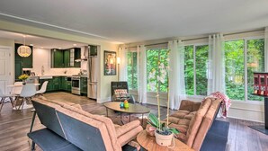 Cocina moderna con armarios verdes, zona de comedor con sofá y mesa, y ventanas amplias con vistas a zonas verdes.