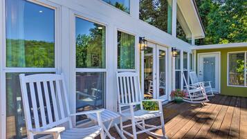 A wooden deck with white rocking chairs and large windows overlooking a garden.
