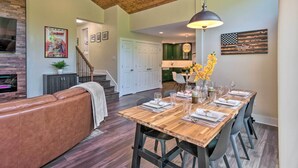 Un salón espacioso con una mesa de comedor de madera dispuesta para seis comensales, un sofá de cuero y una escalera que sube a un nivel superior.