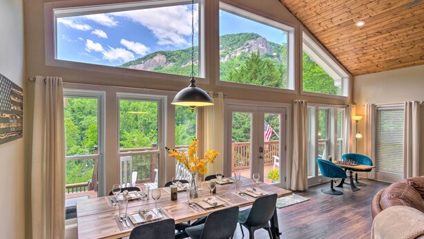 Un comedor espacioso con una mesa de madera dispuesta para cuatro personas, ventanas amplias que ofrecen vistas a las montañas y una zona de estar acogedora con un sofá de cuero.