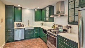 Una cocina moderna con gabinetes verdes, electrodomésticos de acero inoxidable y salpicadero de azulejos.