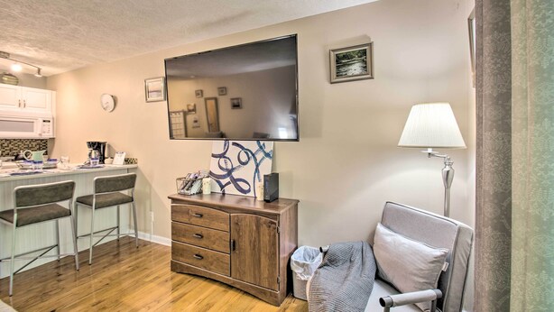 A compact living space with a kitchenette, a flat-screen TV mounted on the wall, a bedside lamp, and a small bedside table. - Wintergreen Resort Studio w/ Deck & Ski-out Access (Nellysford)