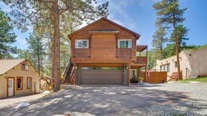 A two-story wooden cabin with a garage, surrounded by trees and a gravel driveway. - Woodland Park Apartment: Forest Views + Deck! (Woodland Park)