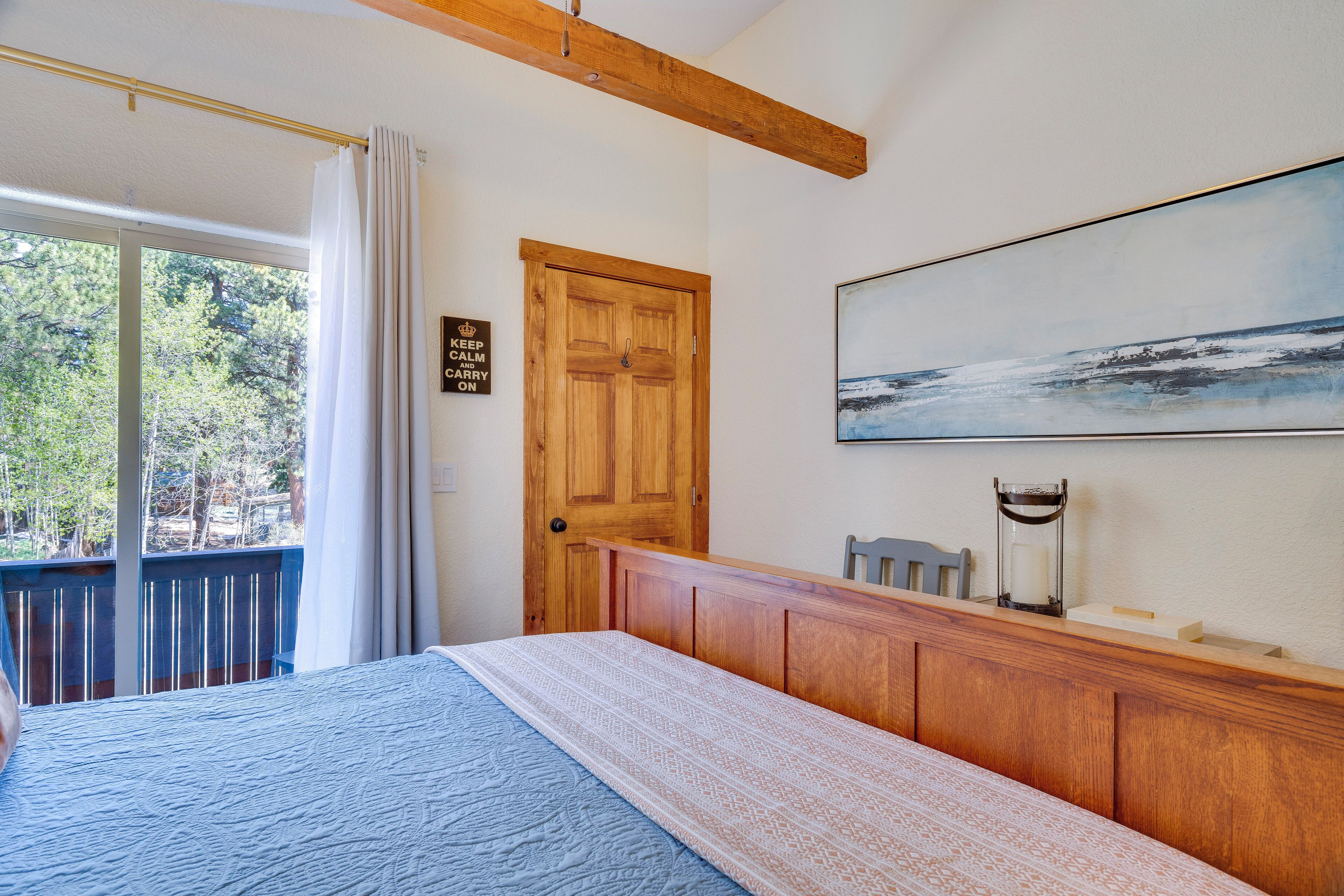 A bedroom with a bed, a wooden headboard, a painting on the wall, a door, and a view of the outdoors.