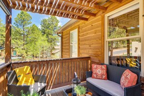 A wooden deck with wicker furniture and a glass door leading to a room. - Woodland Park Apartment: Forest Views + Deck! (Woodland Park)