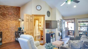 A living room with a stone wall, a white sofa, a grey sofa, a wooden coffee table, and a television. - Woodland Park Apartment: Forest Views + Deck! (Woodland Park)