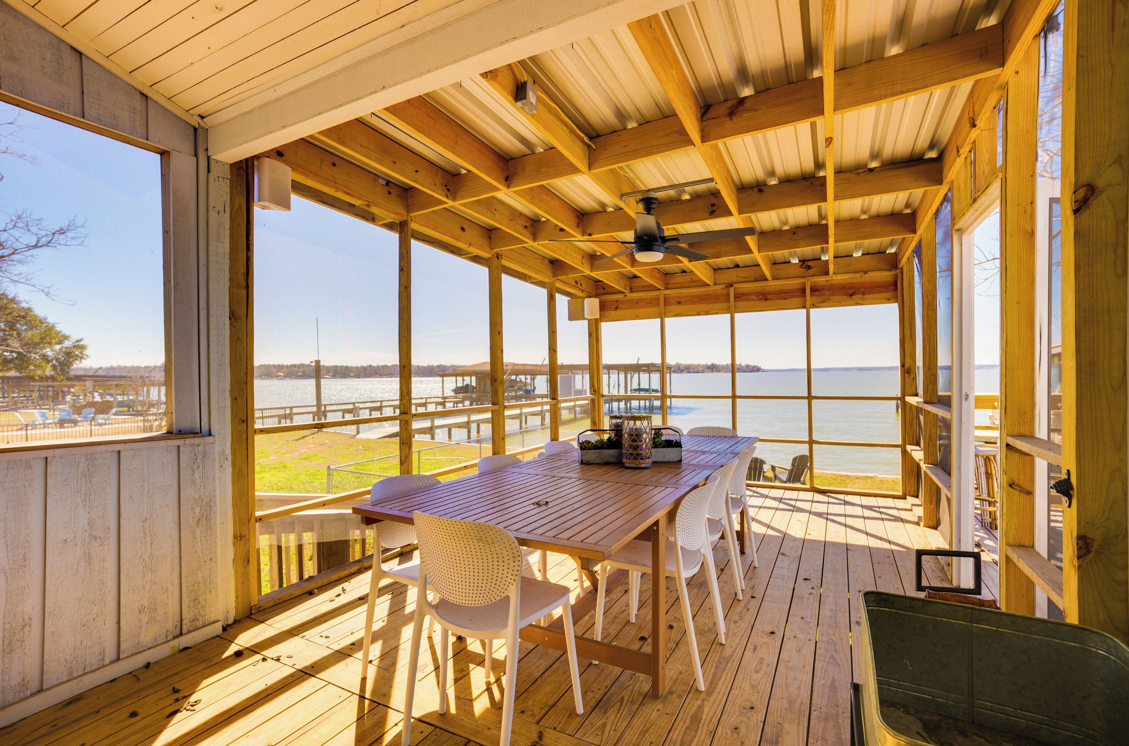 A wooden deck with a table and chairs, overlooking a body of water and a pier.