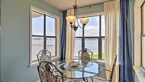 A dining area with a glass table, metal chairs, and a chandelier. - Waterfront Gulf Shores Condo w/ Patio, Pier & Pool (Gulf Shores)
