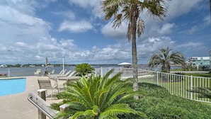 A poolside area with lounge chairs, a palm tree, and a view of the water. - Waterfront Gulf Shores Condo w/ Patio, Pier & Pool (Gulf Shores)