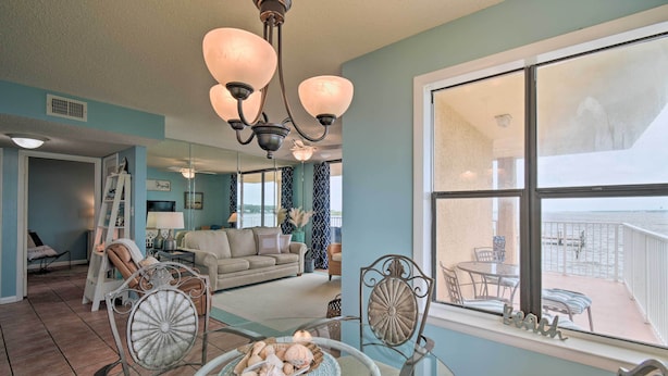 A spacious living room with a view of the beach, a balcony with outdoor furniture, and a chandelier. - Waterfront Gulf Shores Condo w/ Patio, Pier & Pool (Gulf Shores)