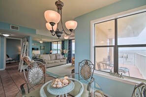 A spacious living room with a view of the beach, a balcony with outdoor furniture, and a chandelier. - Waterfront Gulf Shores Condo w/ Patio, Pier & Pool (Gulf Shores)