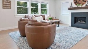 Un salon avec une cheminée, une horloge et une fenêtre donnant sur les arbres.