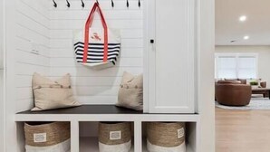 Un banc blanc avec deux coussins et un sac rouge suspendu au plafond. Sous le banc, on trouve trois paniers en osier.