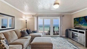 Ett vardagsrum med ett stort fönster, en soffa, en tv och utsikt över havet.
