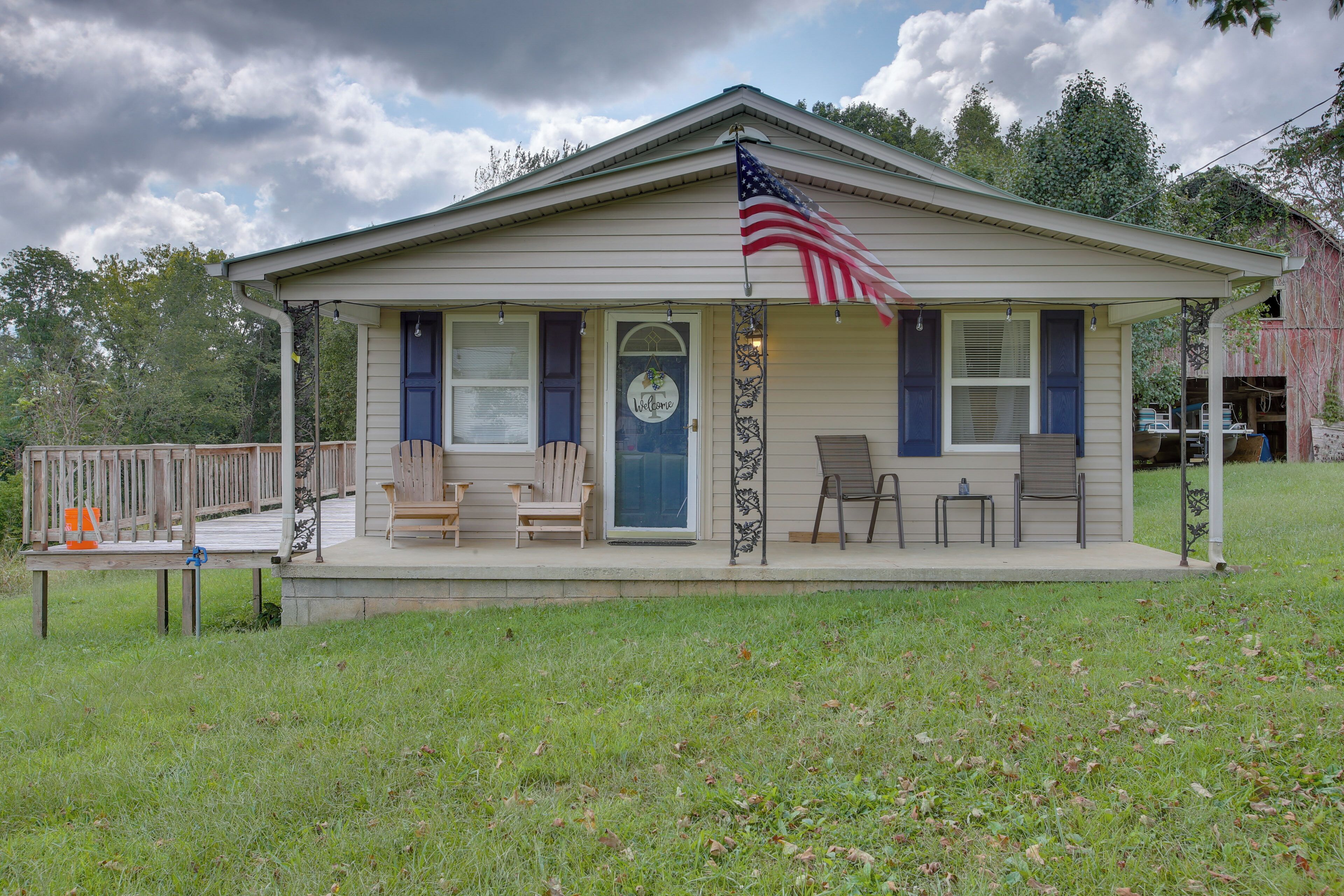 A single-story house with a porch, a welcome sign, and an American flag.