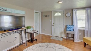 A living room with a flat-screen TV, a coffee table, a chair, a rug, and a door with a fish-shaped decoration. - Albany Family Lake Getaway Near State Parks! (Albany)