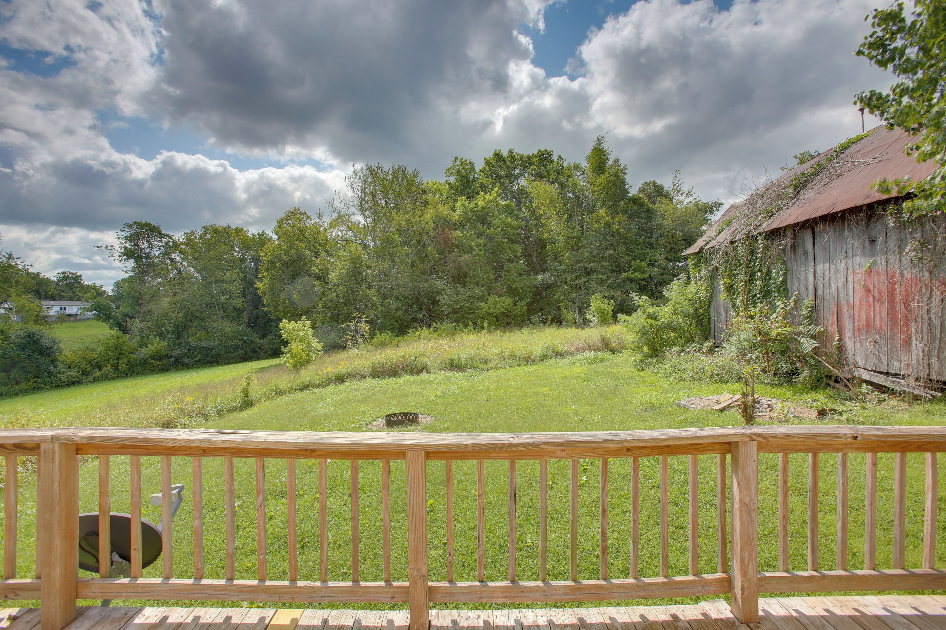 A wooden deck with a view of a grassy field, trees, and a red barn.