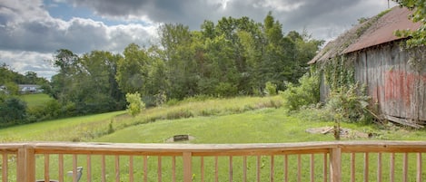 A wooden deck with a view of a grassy field, trees, and a red barn.
