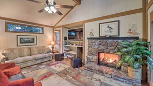 A cozy living room with a stone fireplace, a ceiling fan, a sofa, and a television in the background. - Ski Resort Cabin w/ Deck in Beech Mountain! (Banner Elk)
