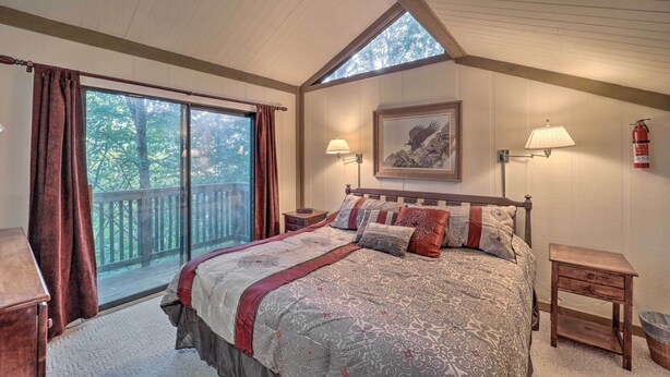 A bedroom with a large bed, a nightstand, a lamp, a framed picture, and a window with curtains. - Ski Resort Cabin w/ Deck in Beech Mountain! (Banner Elk)