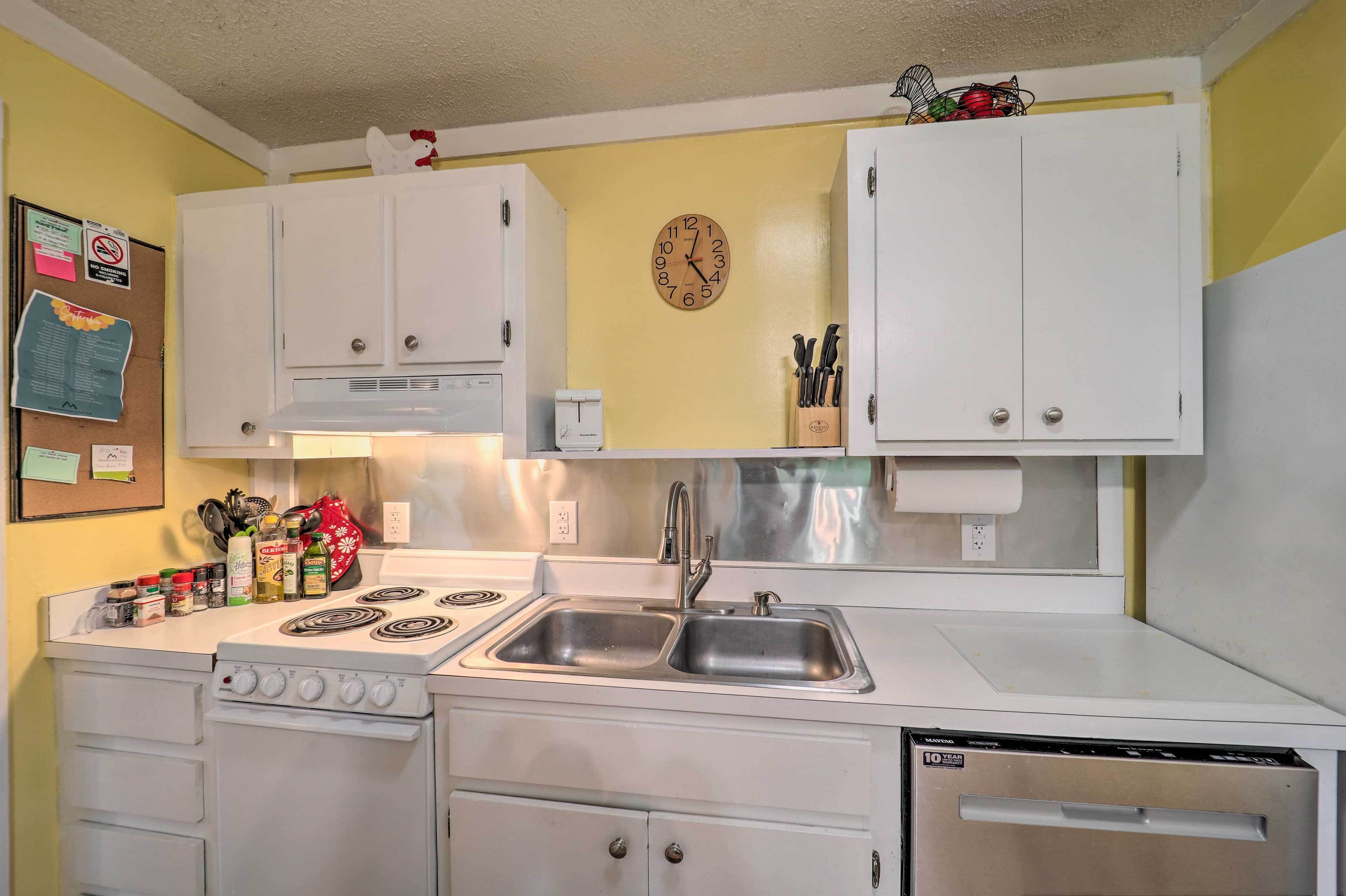 A compact kitchen with white cabinets, a stove, a sink, and a clock on the wall.