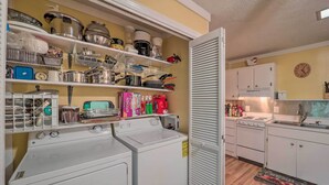 A laundry area with a washing machine, dryer, and shelves with kitchenware and storage containers. - Ski Resort Cabin w/ Deck in Beech Mountain! (Banner Elk)