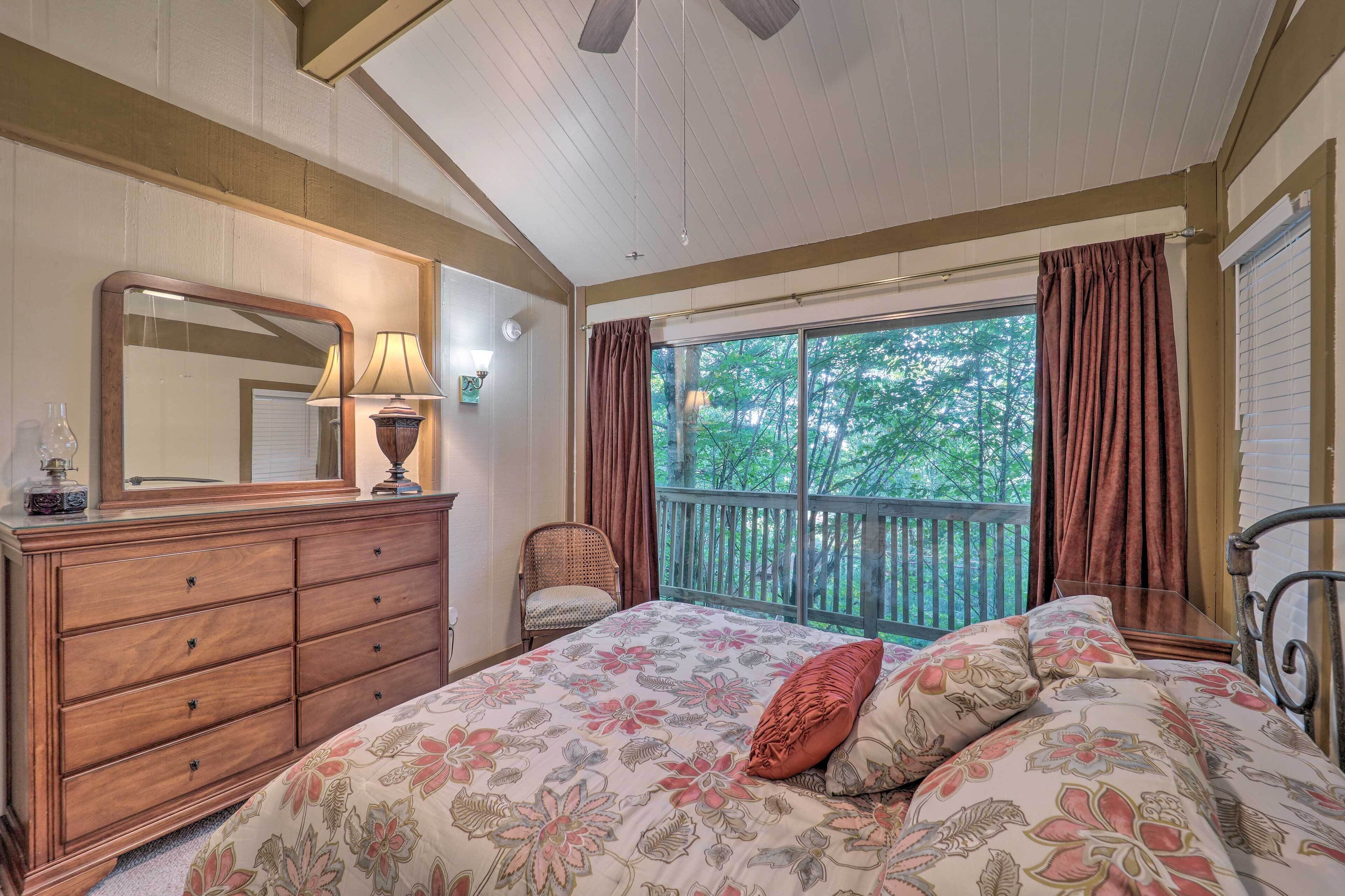 A bedroom with a large bed, a dresser, a mirror, a chair, and a balcony with curtains.