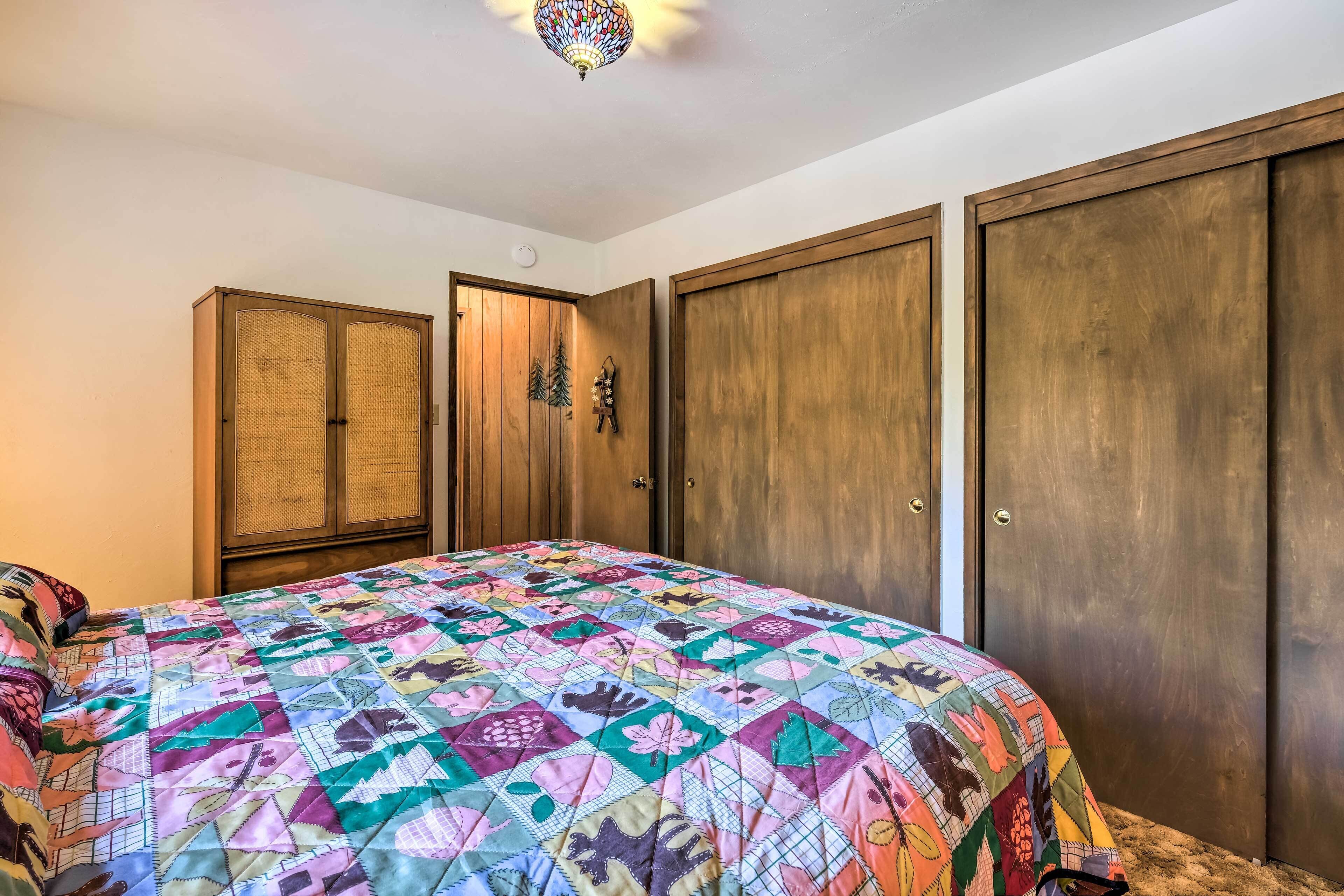 Une chambre à coucher avec une couverture colorée, une armoire en bois et un luminaire fixé au plafond.