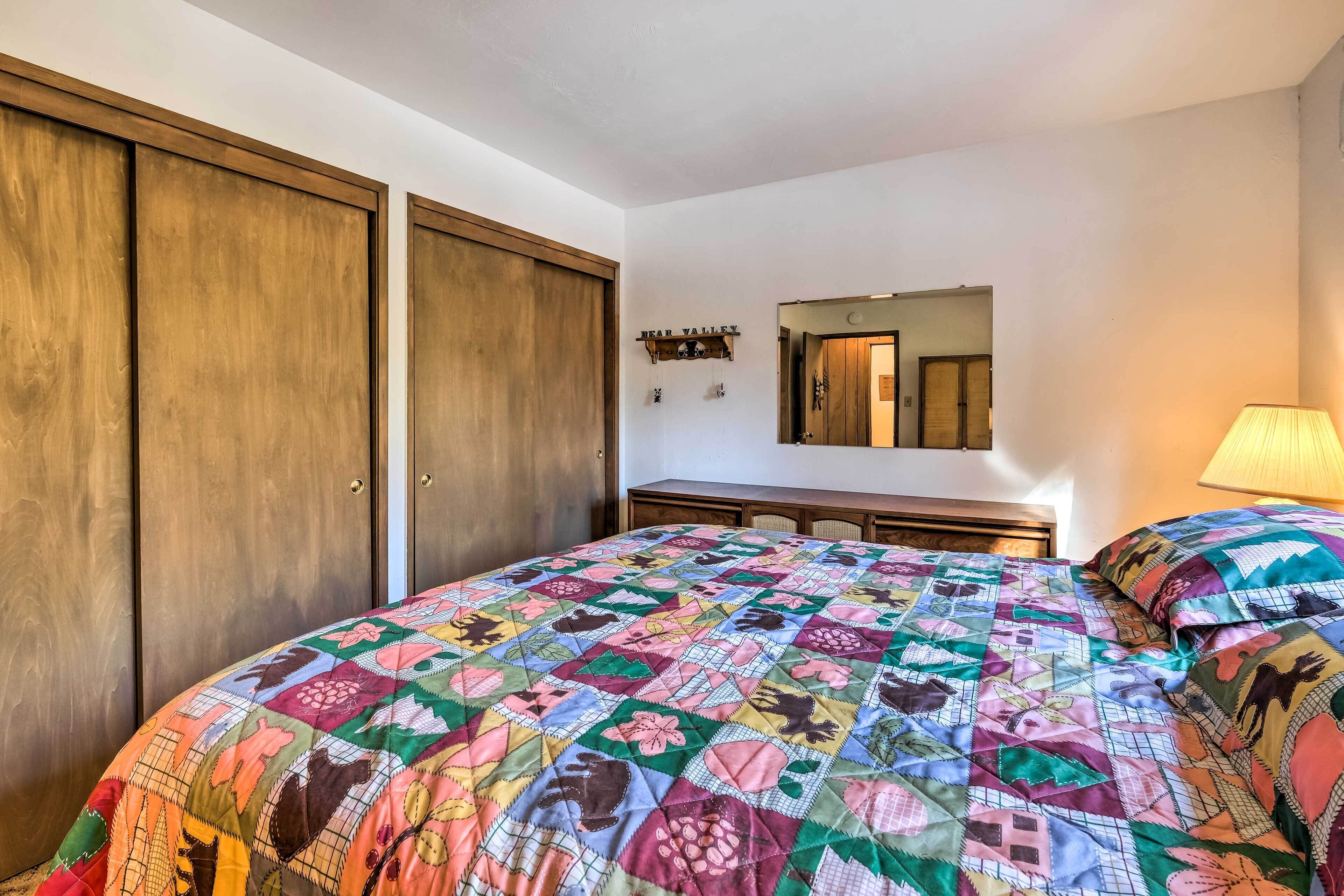 Un dormitorio con una cama grande, armario de madera, cómoda, espejo y estante con un cartel.