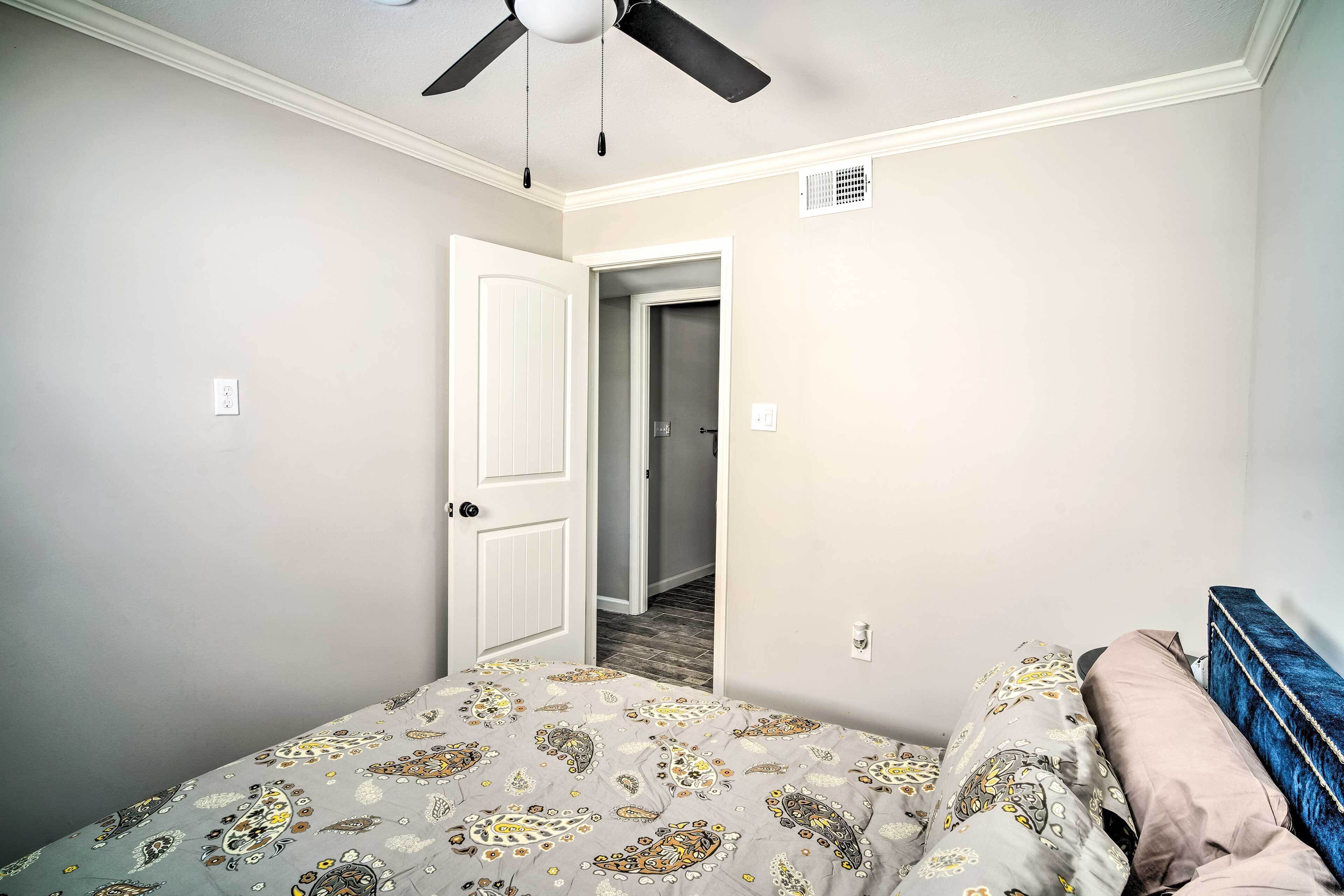 A bedroom with a bed, a door, a ceiling fan, and a wall-mounted light switch.
