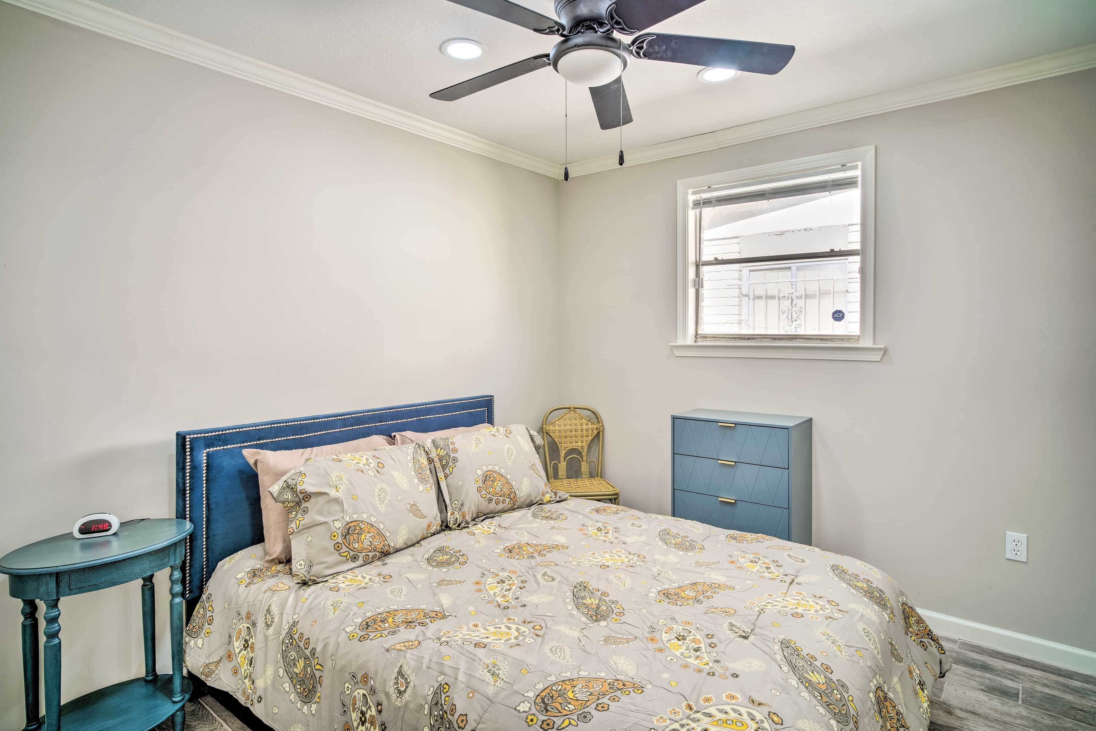 A bedroom with a bed, a nightstand, a dresser, a ceiling fan, and a window.
